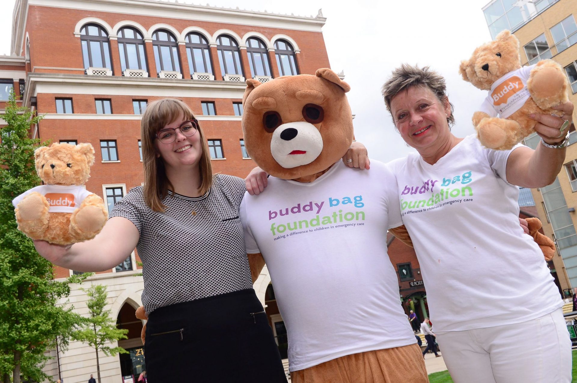 Two women hugging a person in a bear costume in Brindleyplace, Birmingham.