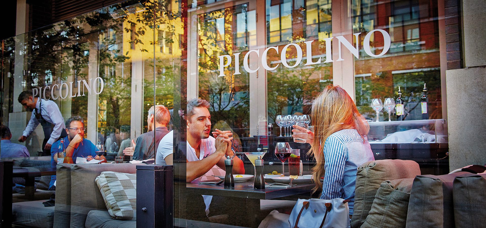 Two people eating and drinking through the window of Piccolino in Birmingham.