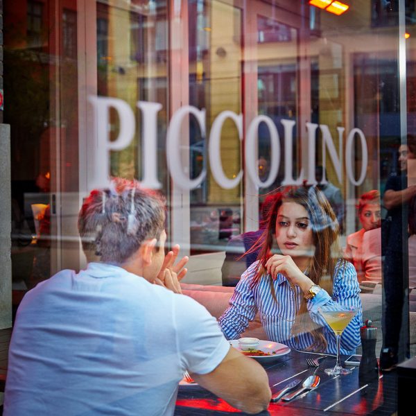 Two people eating and drinking through the window of Piccolino in Birmingham.