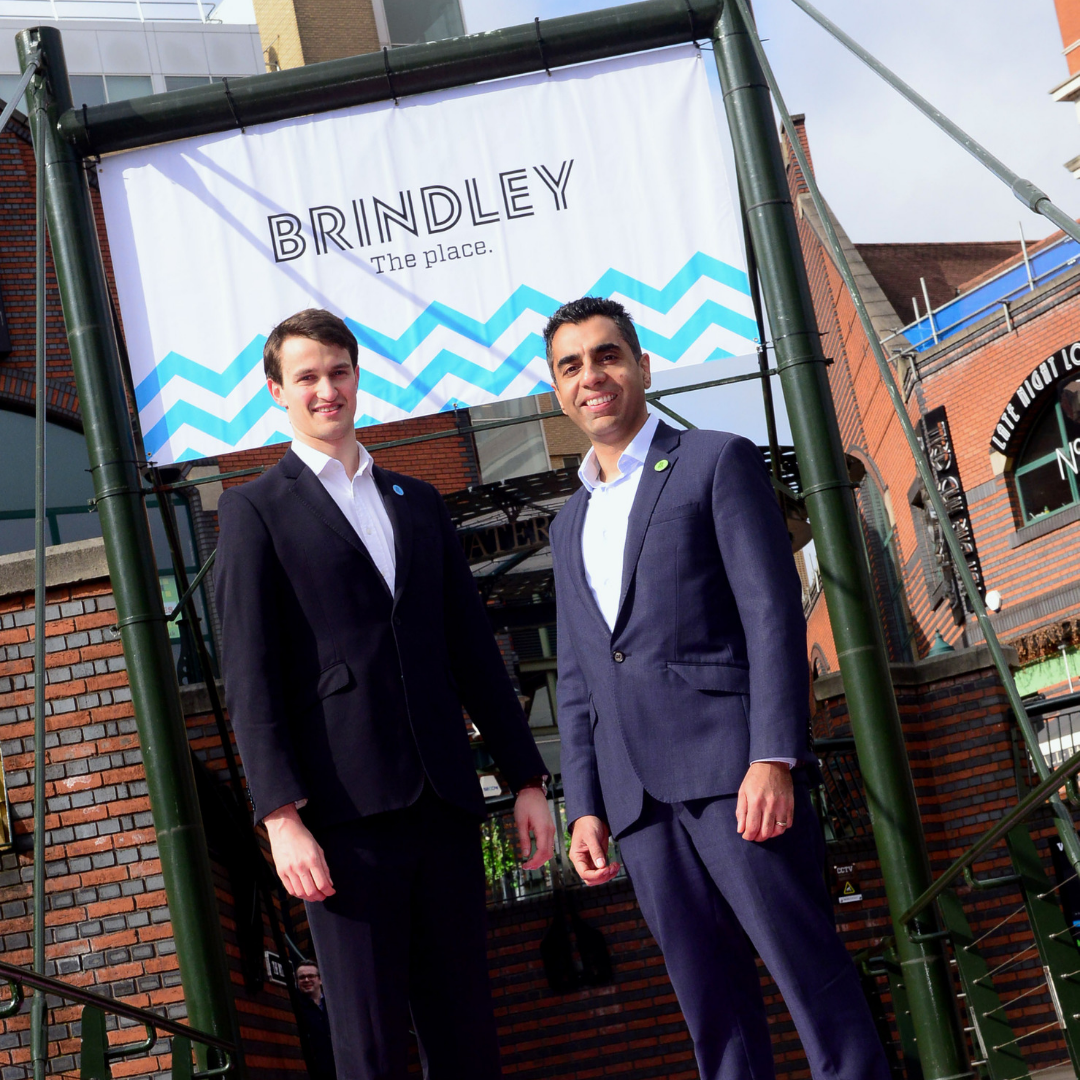 Two men in suits standing in front of signage at Brindleplace in Birmingham.