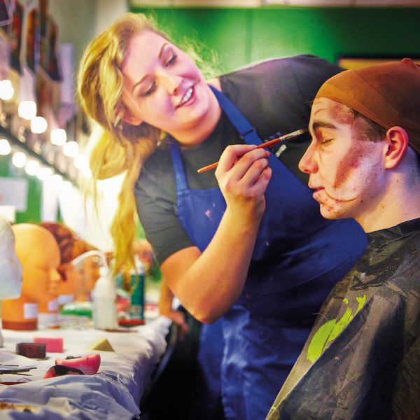 Woman applying theatrical makeup to a man at the Crescent Theatre in Birmingham.