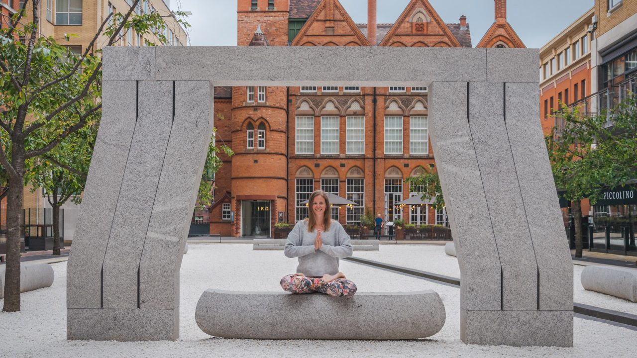 Yoga instructor sitting under the arch in Oozells Square at Brindleyplace.