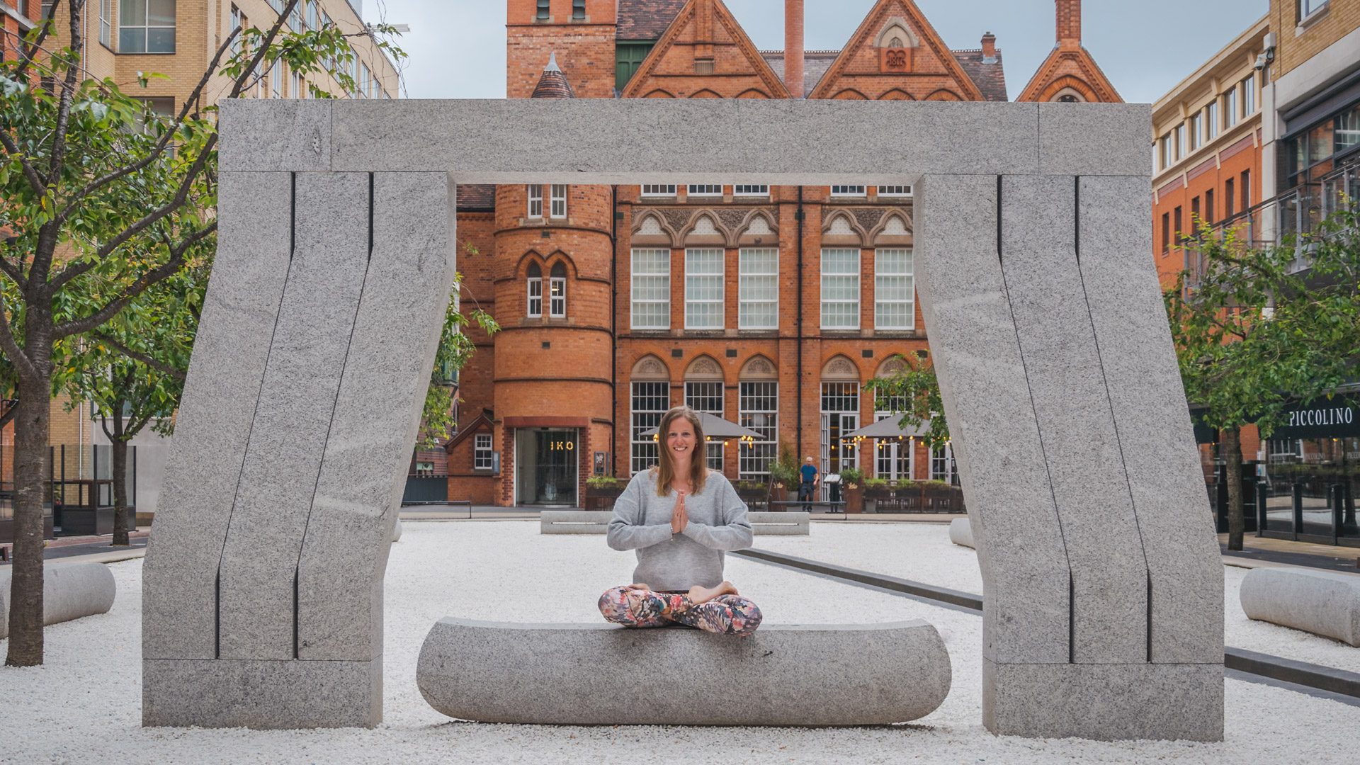 Yoga instructor sitting under the arch in Oozells Square at Brindleyplace.