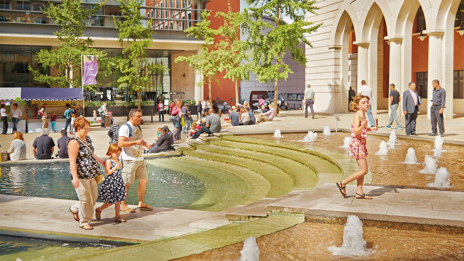 Family walking across the fountains in Central Square at Brindleyplace.