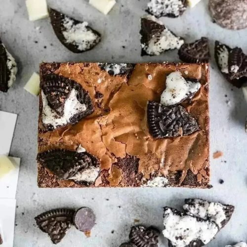 A close up of an Oreo brownie from Beeston Brownie surrounded by Oreo chunks on a grey background.