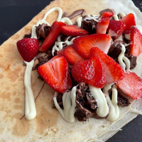 A close up of a crepe with strawberries, chocolate and a sweet white sauce.