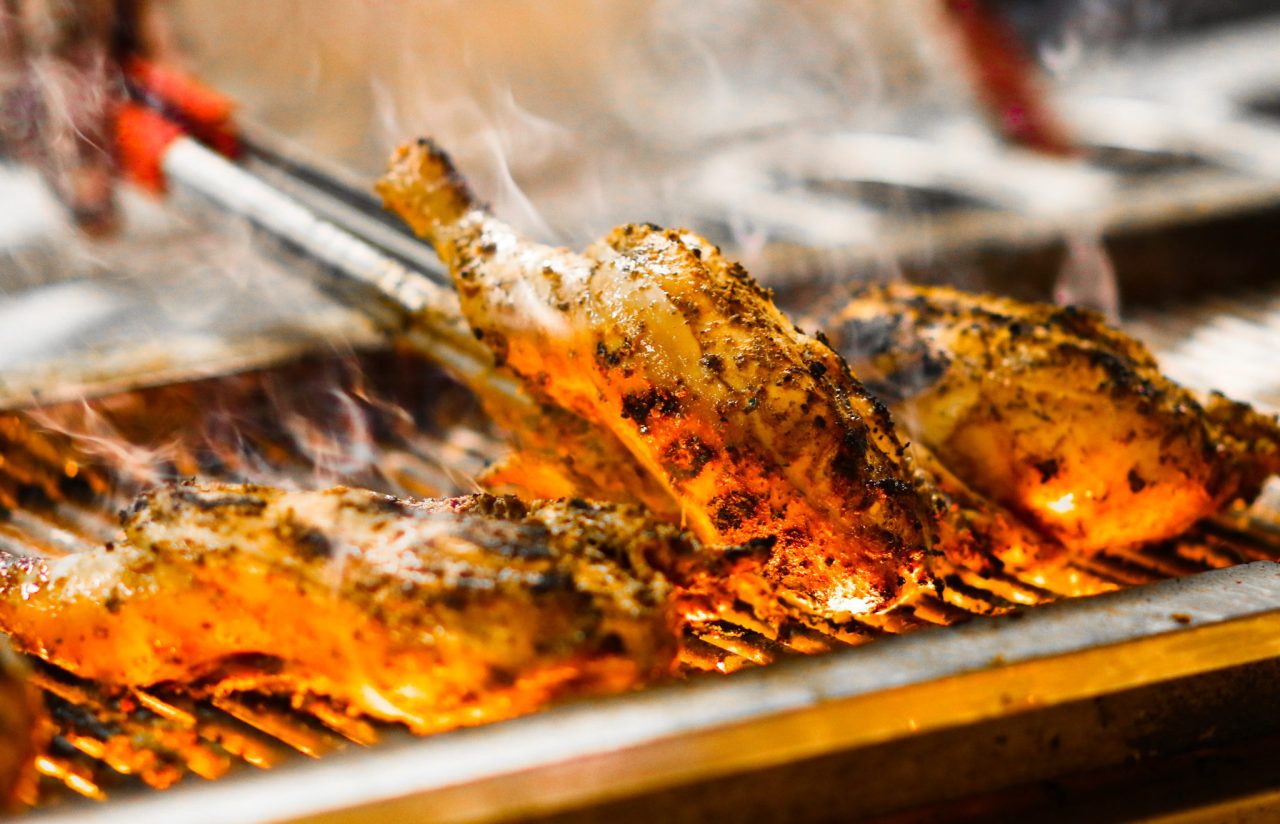 Turtle Bay Jerk Chicken on the grill. One piece is being flipped over with tongs.