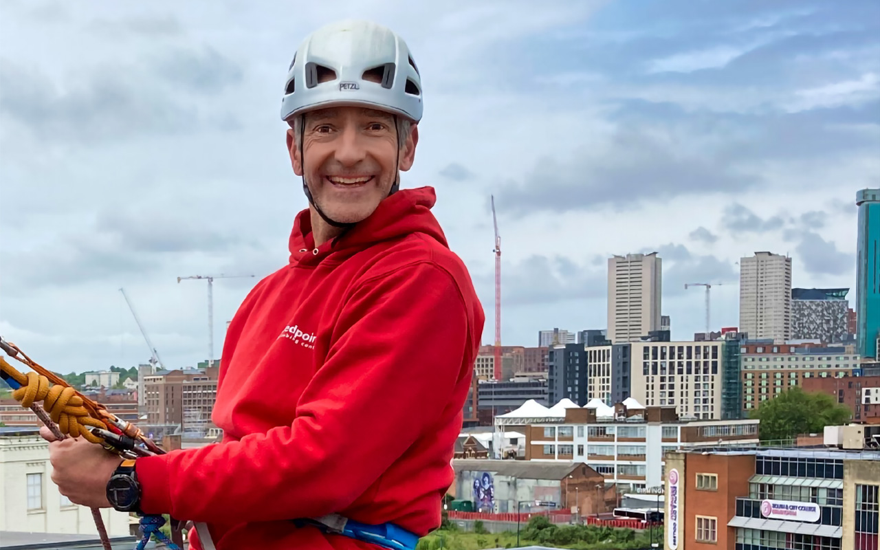 Man abseiling down building. Birmingham skyline is visible in background.