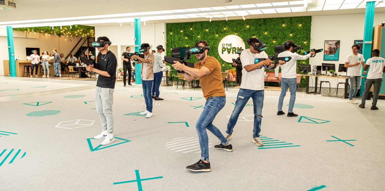 Players wearing VR headsets and holding gun shaped controllers in a large open room. The Park VR experience at Brindleyplace Birmingham.