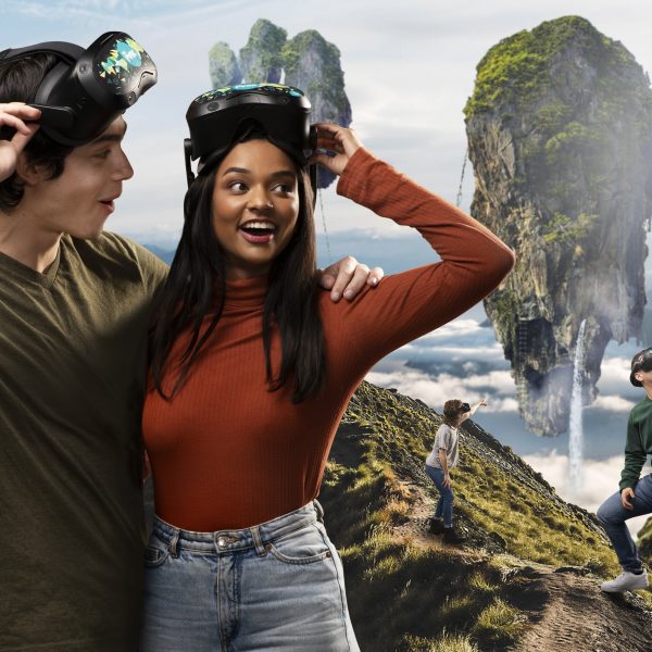 A man and a woman stand with the arms around eachother with VR goggles moved onto their heads as the look at a fantastical landscape of floating islands and waterfalls.