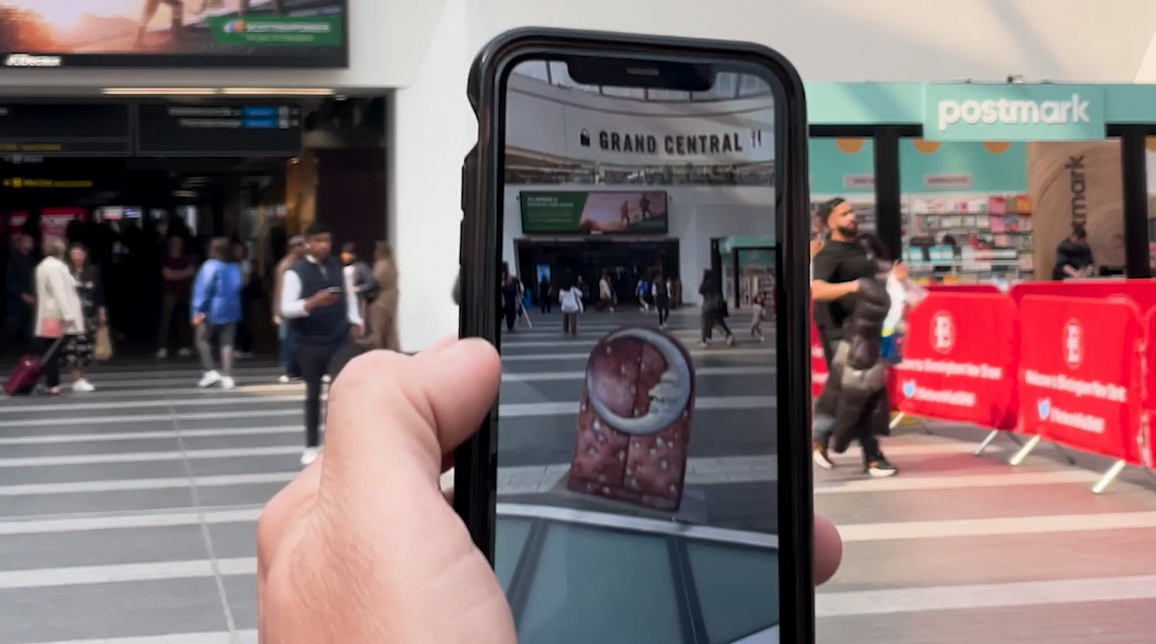 A photo of someone holding a phone while a augmented reality image of a crescent moon Birmingham Royal Ballet The Nutcracker prop is shown on the phone screen.
